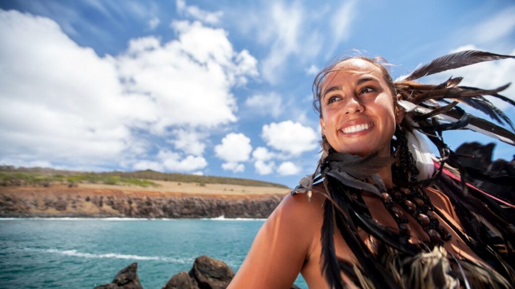 Legacy of Rapa Nui - easter island Smiling Rapa Nui woman wearing traditional feather adornments by the coast of Easter Island, symbolizing cultural pride and heritage.