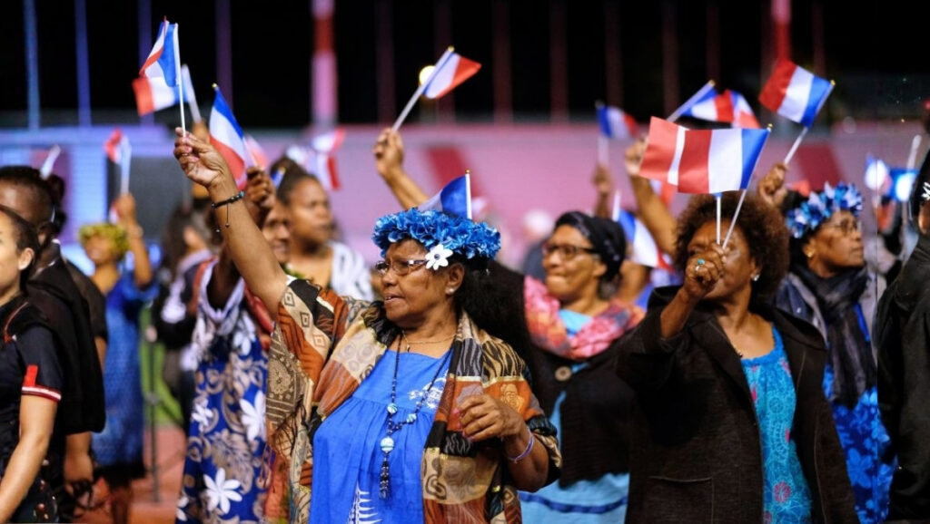 Women in New Caledonia wave French flags during celebrations following the Nouméa Accord independence referendums, showing unity and national pride.