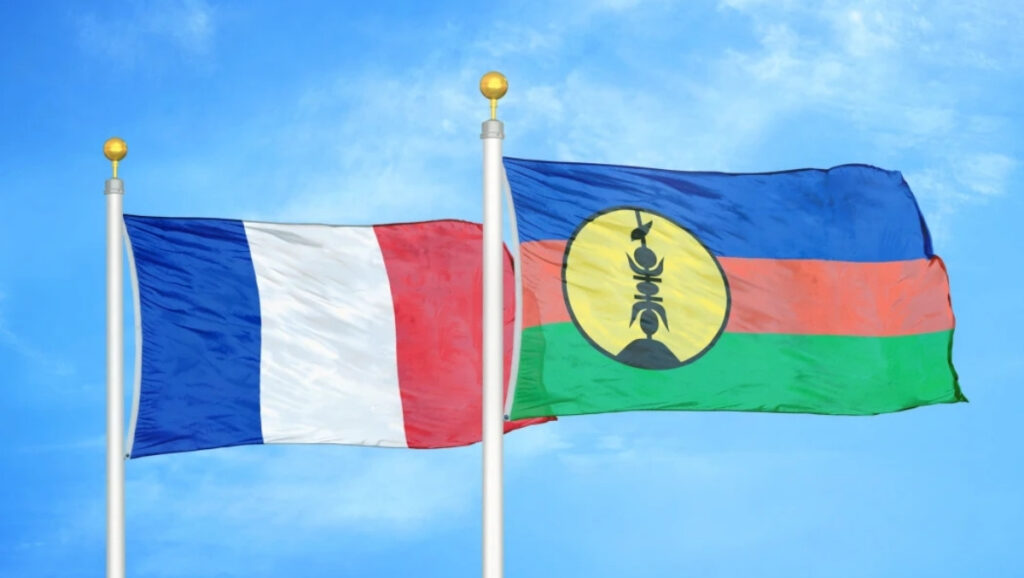 French and New Caledonian flags flying side by side against a bright blue sky, symbolizing unity and shared identity.