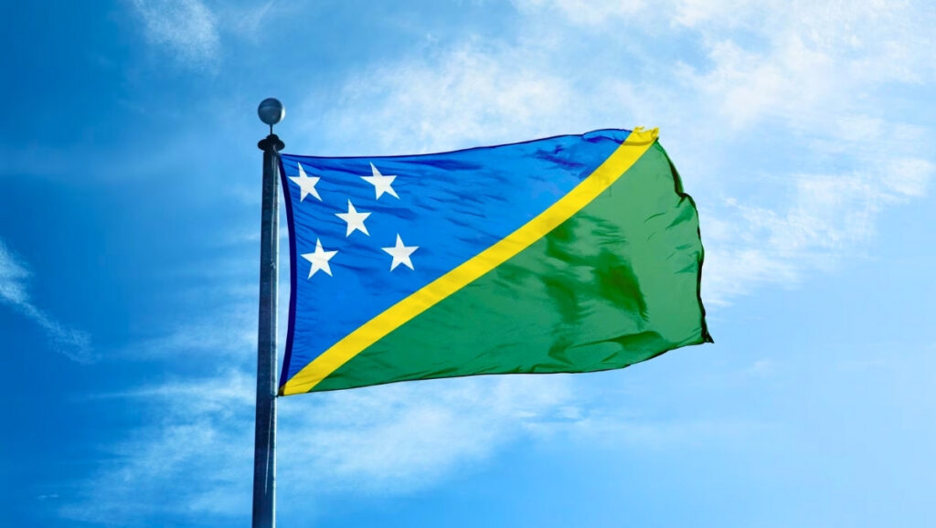 National flag of the Solomon Islands waving under a blue sky, its five white stars
