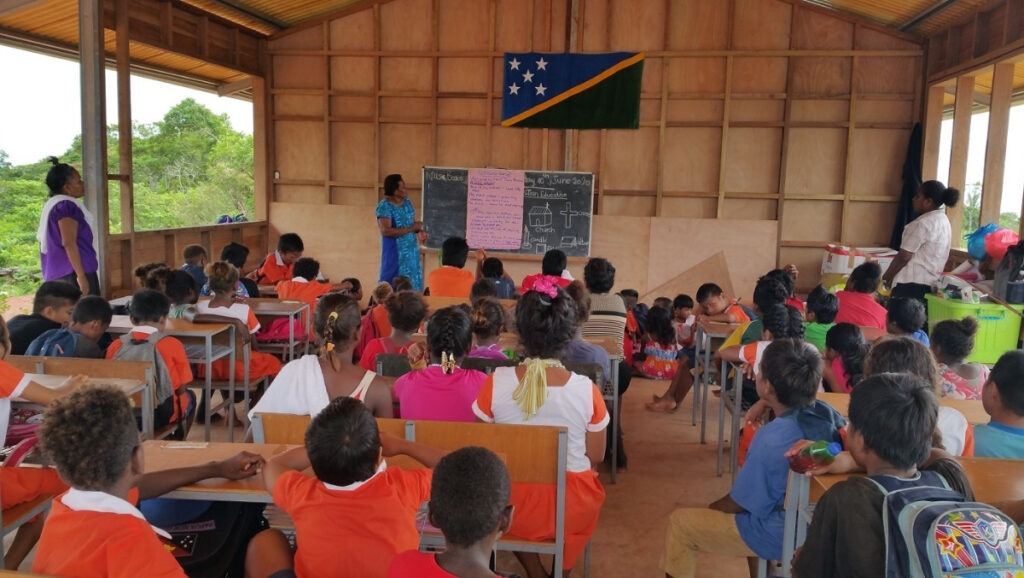 Teacher and students in a Solomon Islands classroom under the national flag.