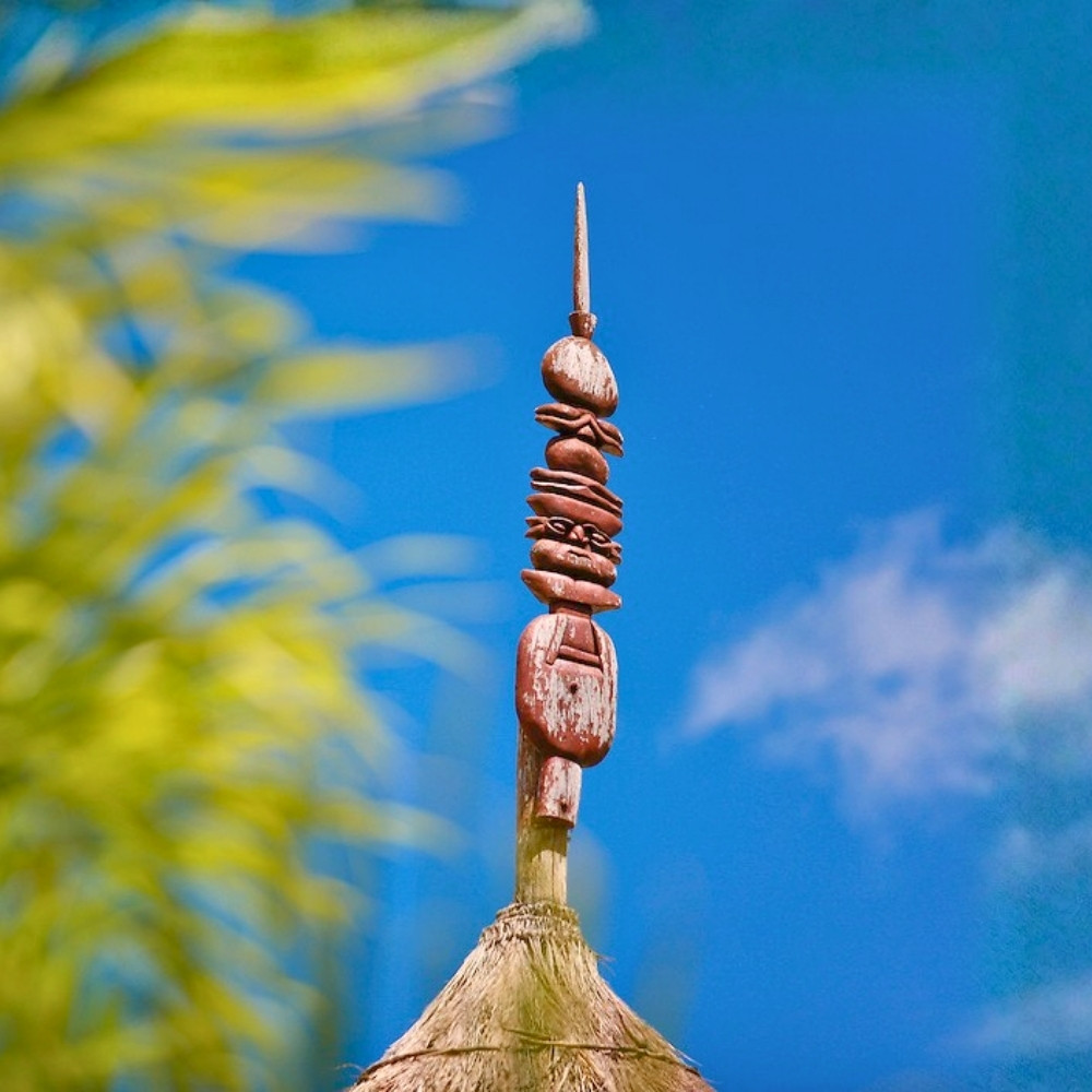 Traditional Kanak flèche faîtière carved wooden totem atop a hut roof in New Caledonia, symbolizing ancestral protection and cultural heritage.