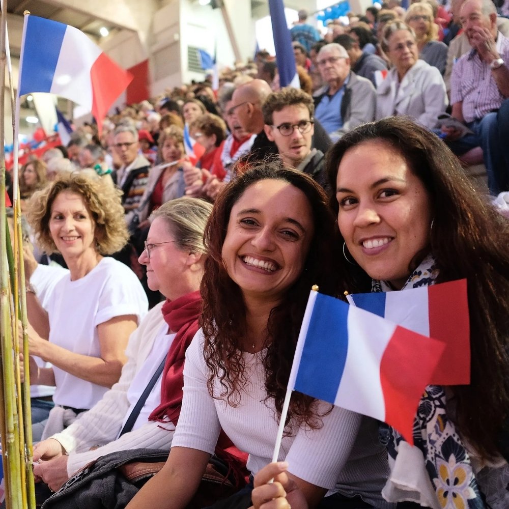 People in New Caledonia smiling and waving French flags at an event, reflecting the territory’s French influence and official use of the French language.