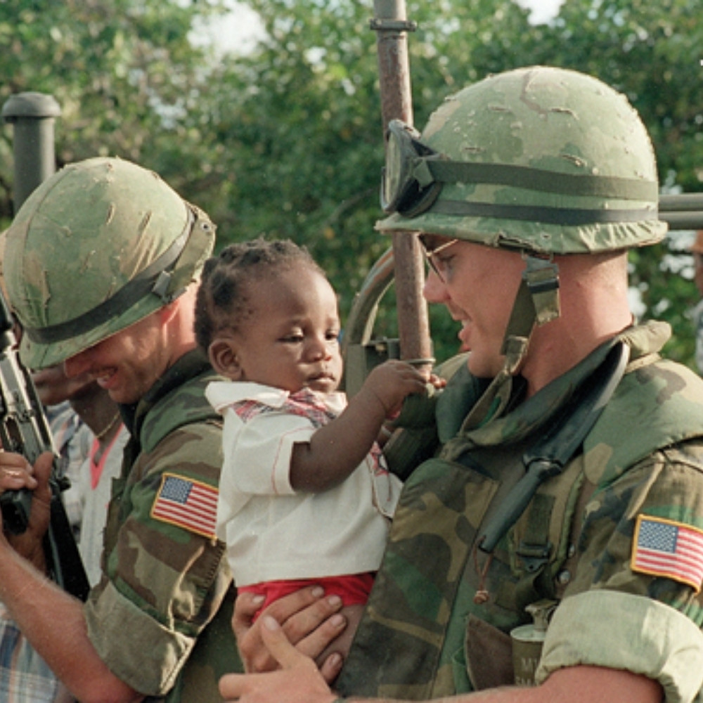 Collection 23 - thanksgiving Soldiers in uniform gently assisting a small child, symbolizing humanitarian support linked to Grenada’s 1983 Thanksgiving remembrance.