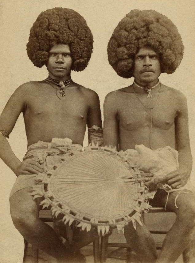 Historical portrait of two Indigenous Melanesian men from New Caledonia, wearing traditional ornaments and holding a woven cultural artifact.