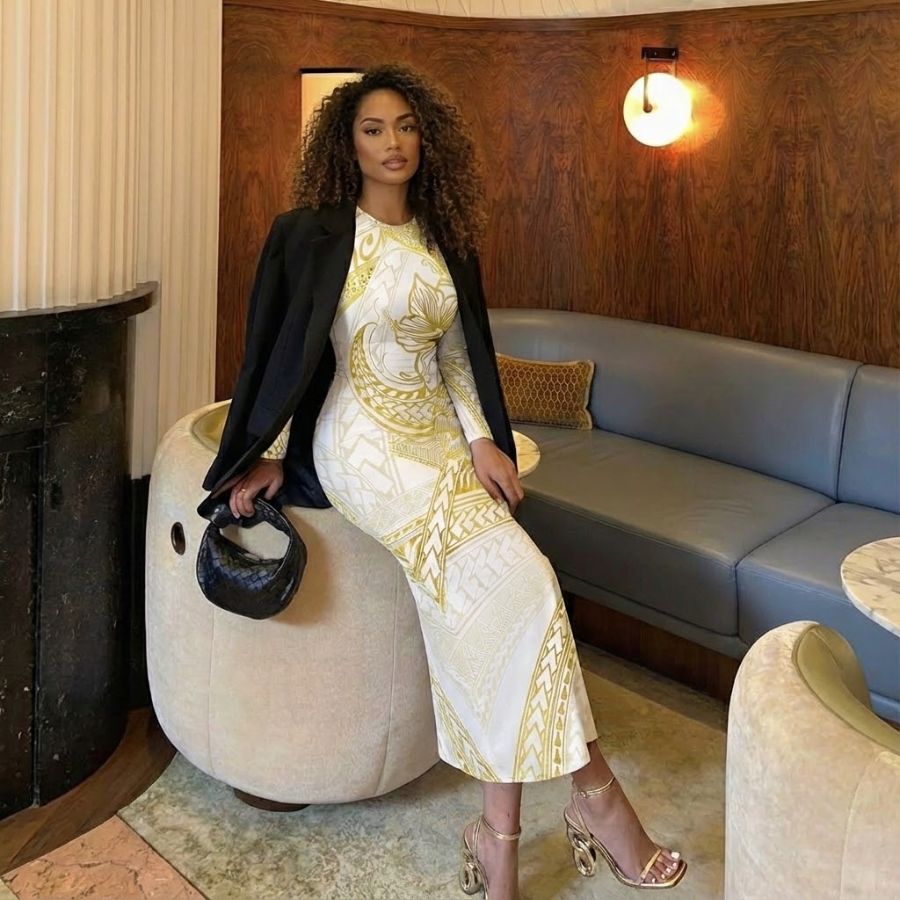 polynesian woman wearing white and gold patterned sleeveless bodycon midi dress with black blazer and heels, sitting in modern lounge