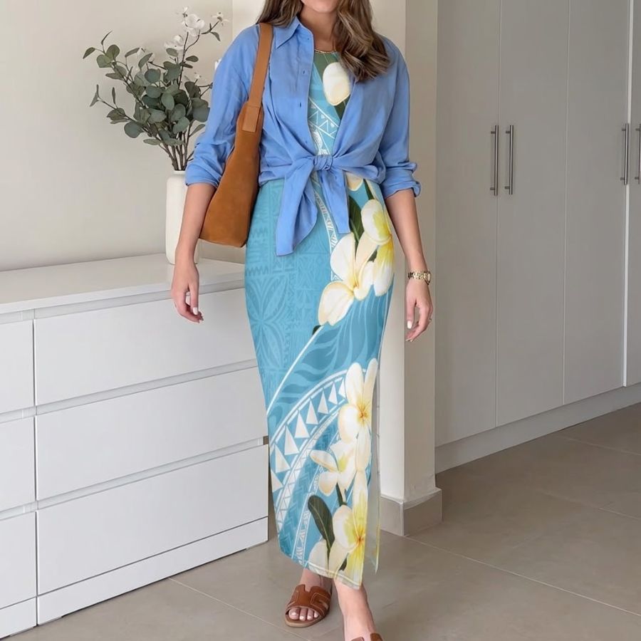 Woman wearing blue tropical floral bodycon maxi dress with white plumeria print, styled with light blue shirt, tan tote bag and sandals in bright bedroom