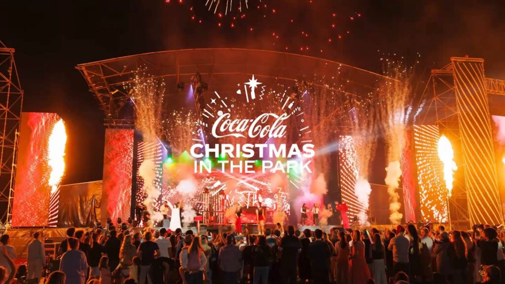 Crowd watching a large outdoor Christmas concert with fireworks and bright stage lights at Coca-Cola Christmas in the Park in New Zealand.