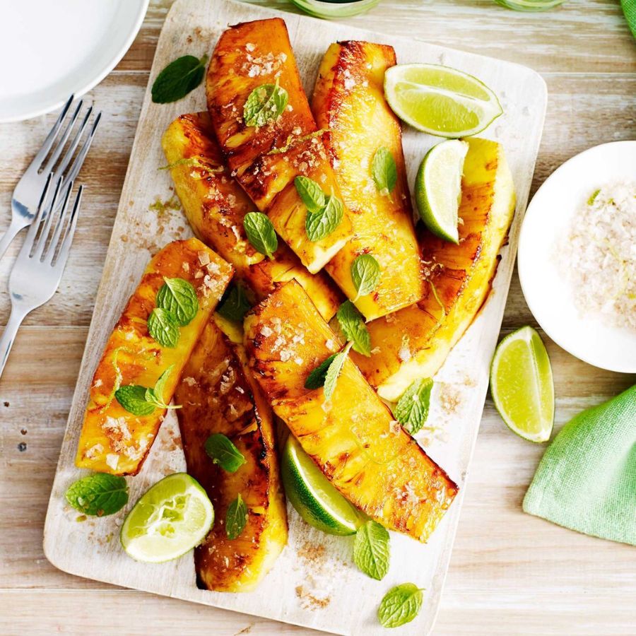 Grilled pineapple wedges on wooden board served with fresh lime slices and mint leaves