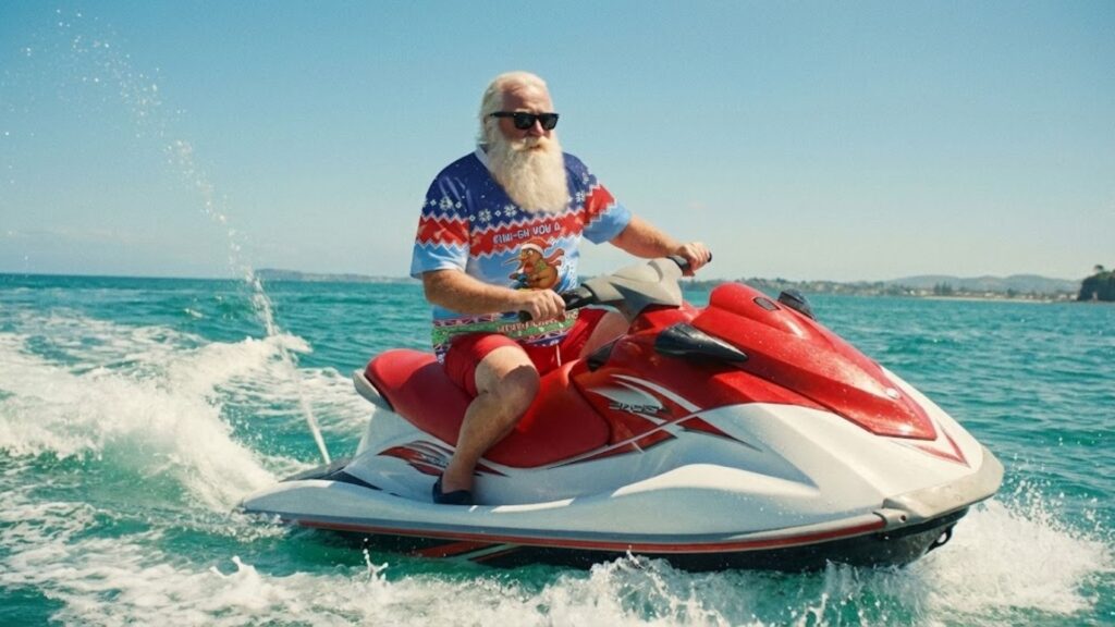A Kiwi-style Santa riding a jet ski on the ocean in New Zealand, wearing summer clothes and embracing the iconic summer Santa New Zealand vibe.